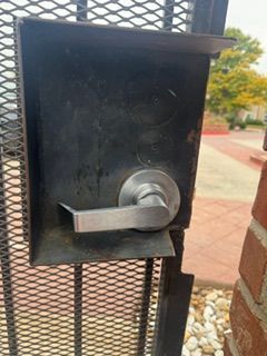 Close-up of a black metal door latch on a mesh gate outdoors.