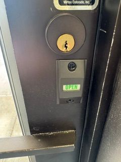 Close-up of a black door with a keypad lock and glowing green “OPEN” sign.