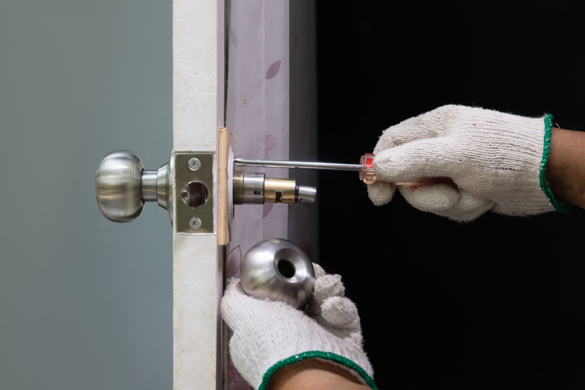 Hands in white gloves using a screwdriver to install a silver door lock.