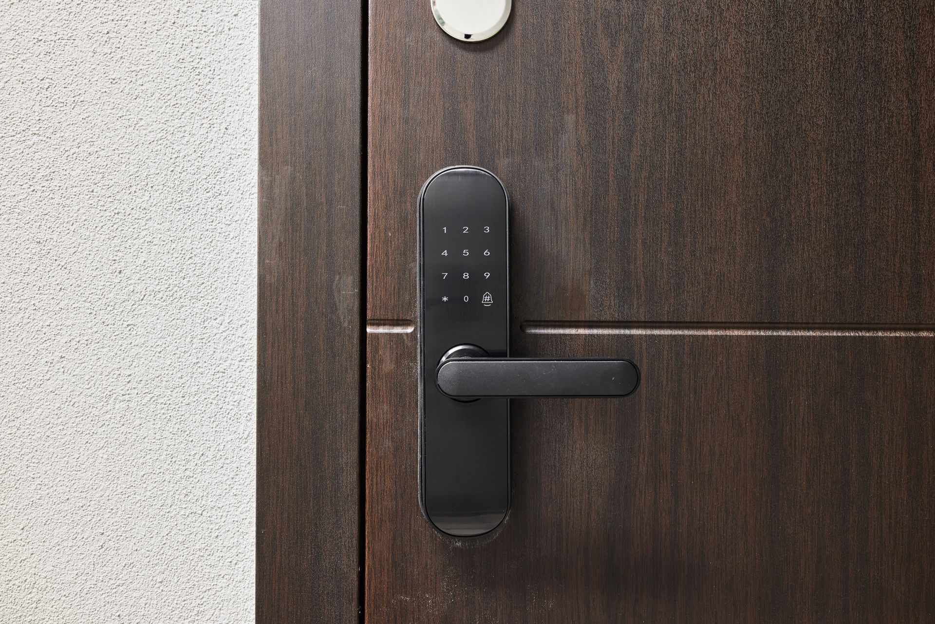 Black electronic door handle on a dark wooden door beside a light textured wall.