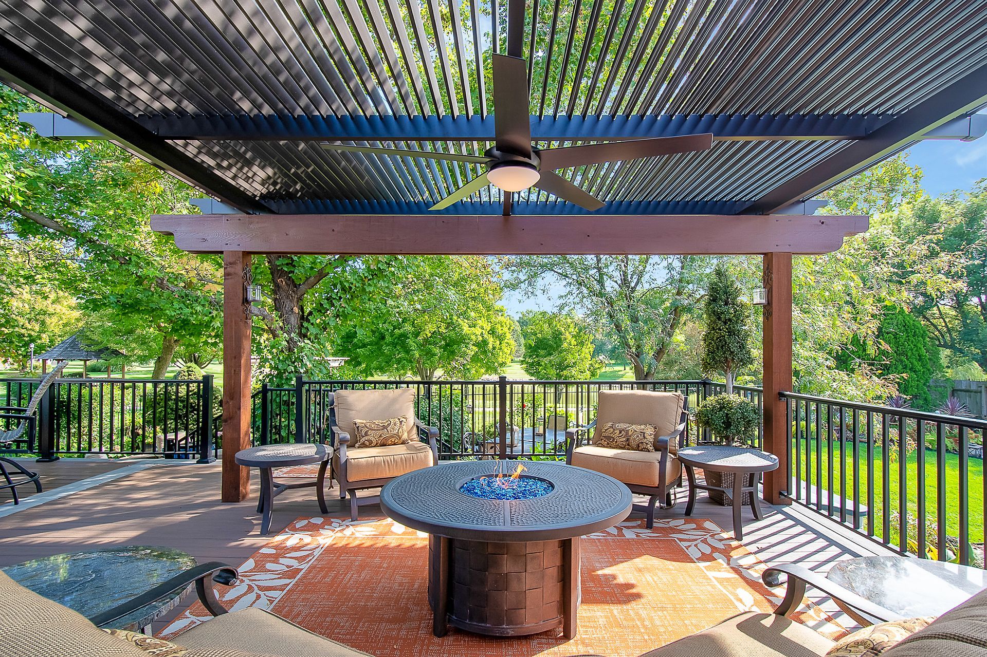 A patio with a fire pit , chairs , tables and a ceiling fan.