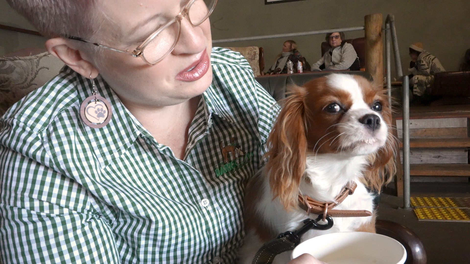 A woman is holding a small brown and white dog next to a cup of coffee.