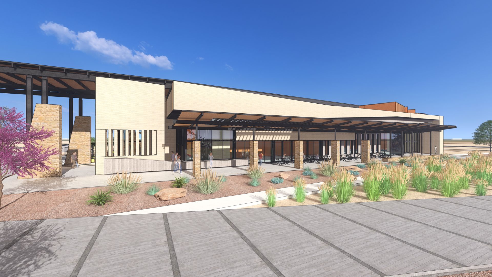 Modern building with covered entrance and parking area, landscaped with desert plants, under a blue sky.