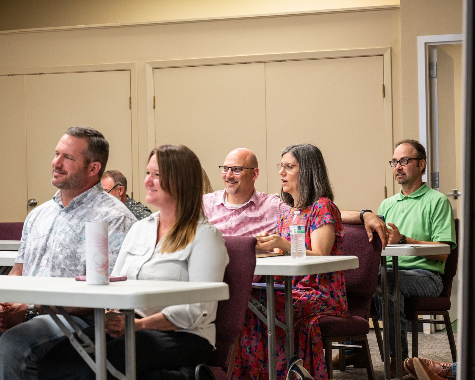 People seated at tables in a room, watching something.