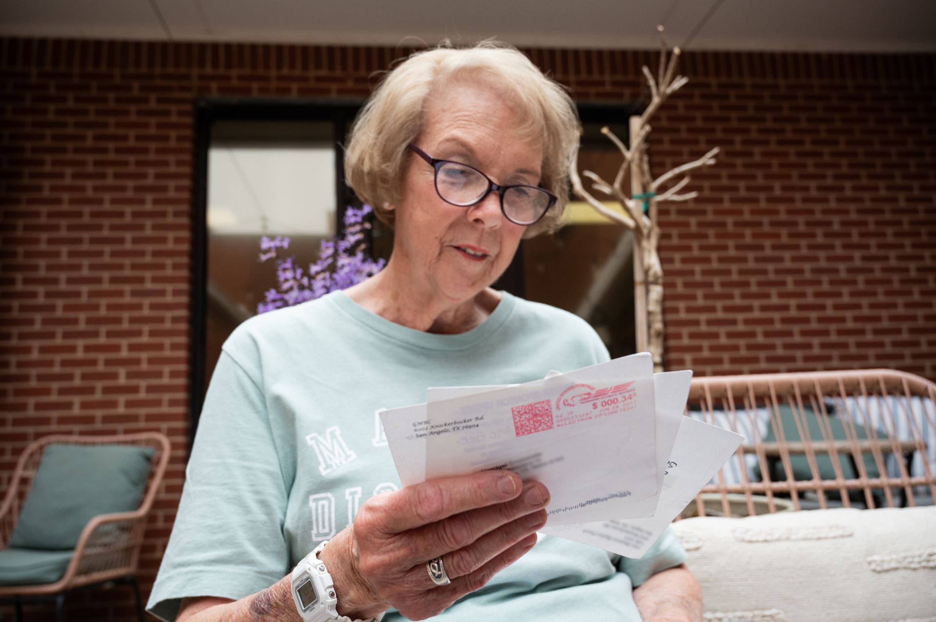Woman in a mint sweater reading letters outdoors on a patio with brick walls and wicker furniture