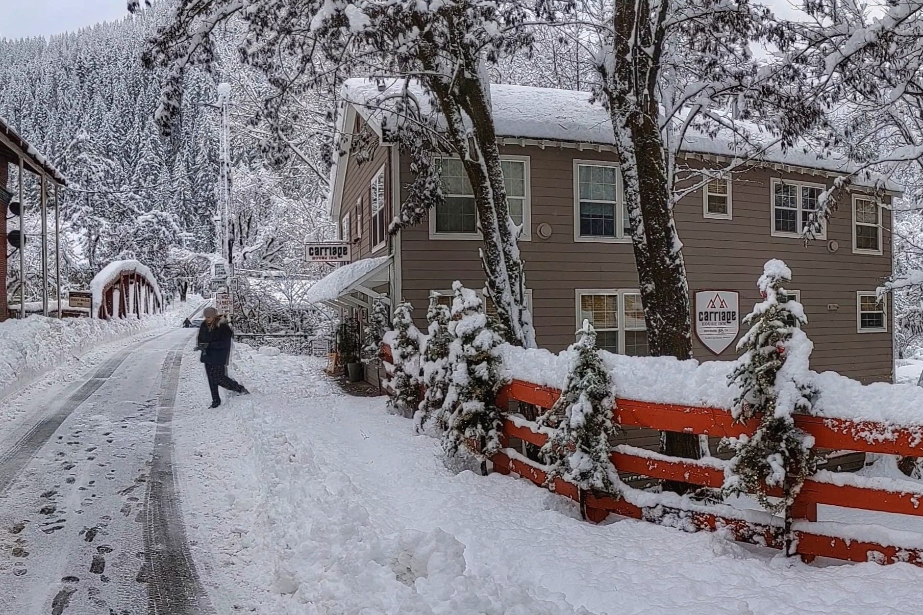A person is walking down a snowy road in front of a house