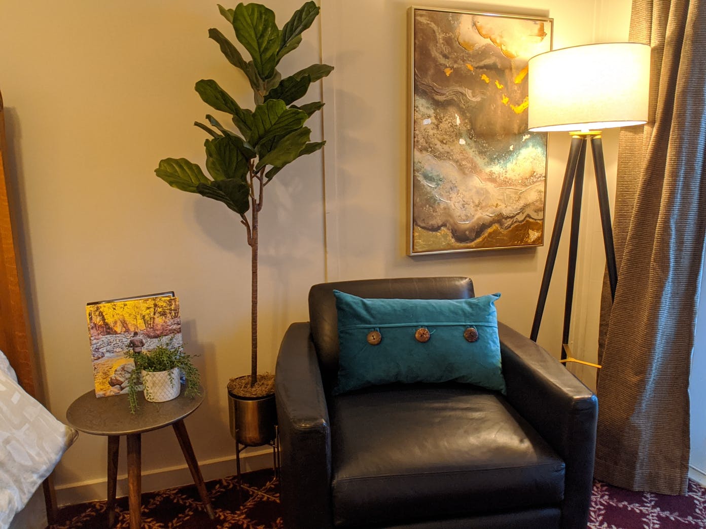 A living room with a chair , lamp , table and painting on the wall.