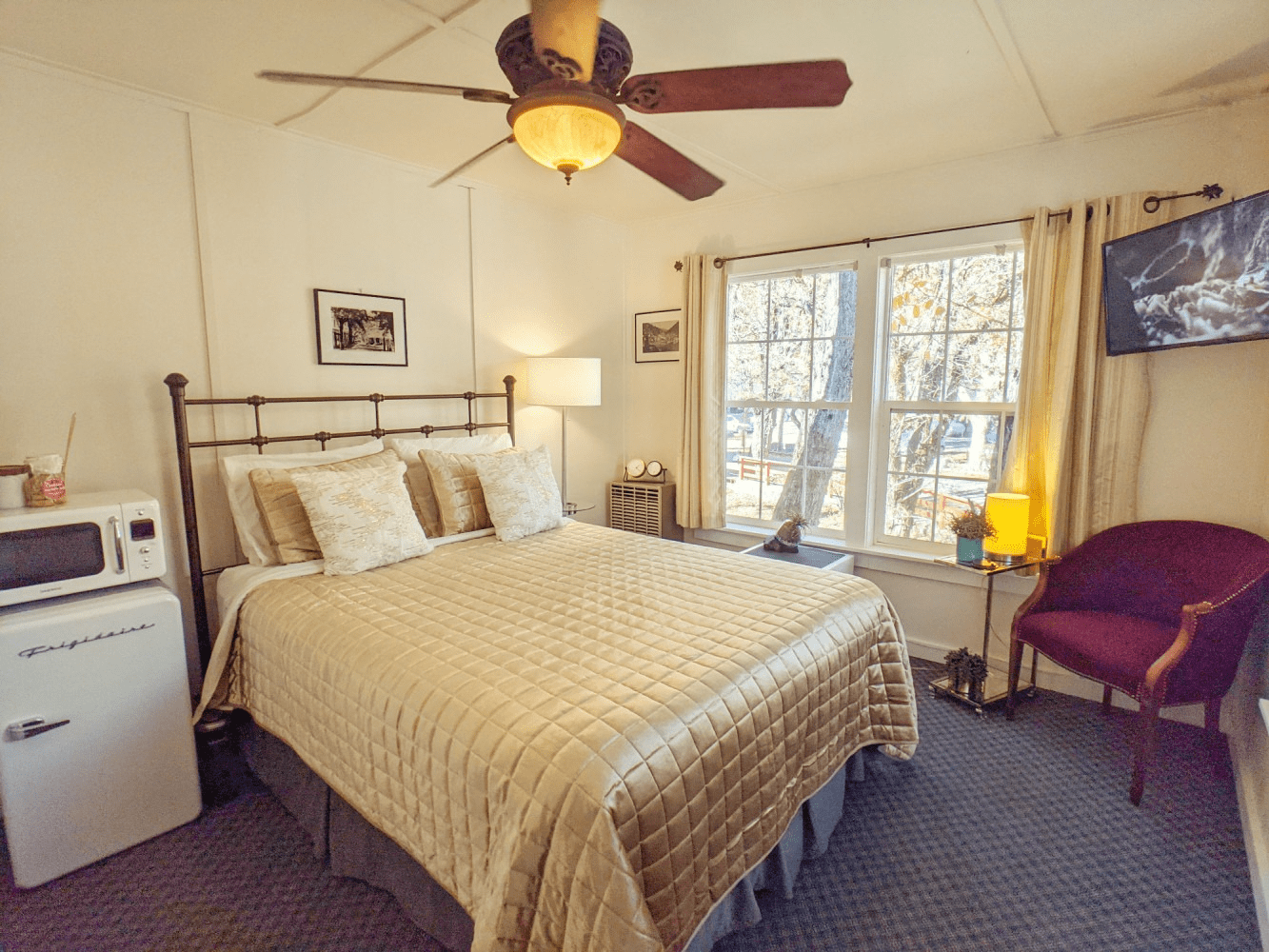 A bedroom with a bed , chair , microwave and ceiling fan.