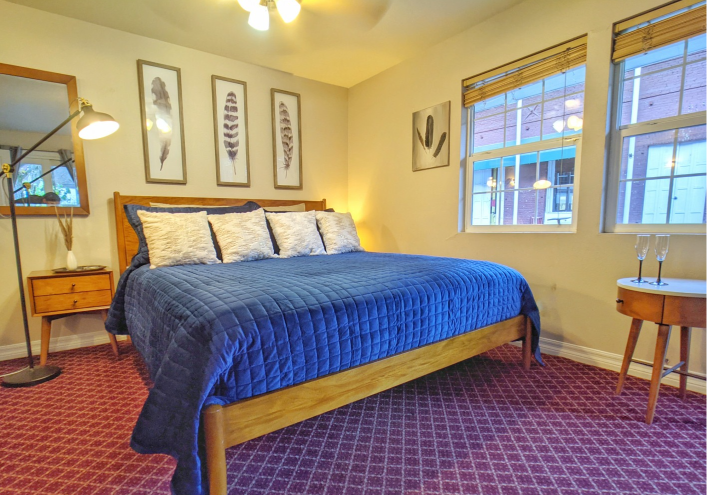 A bedroom with a king size bed , two windows , a nightstand and a mirror.