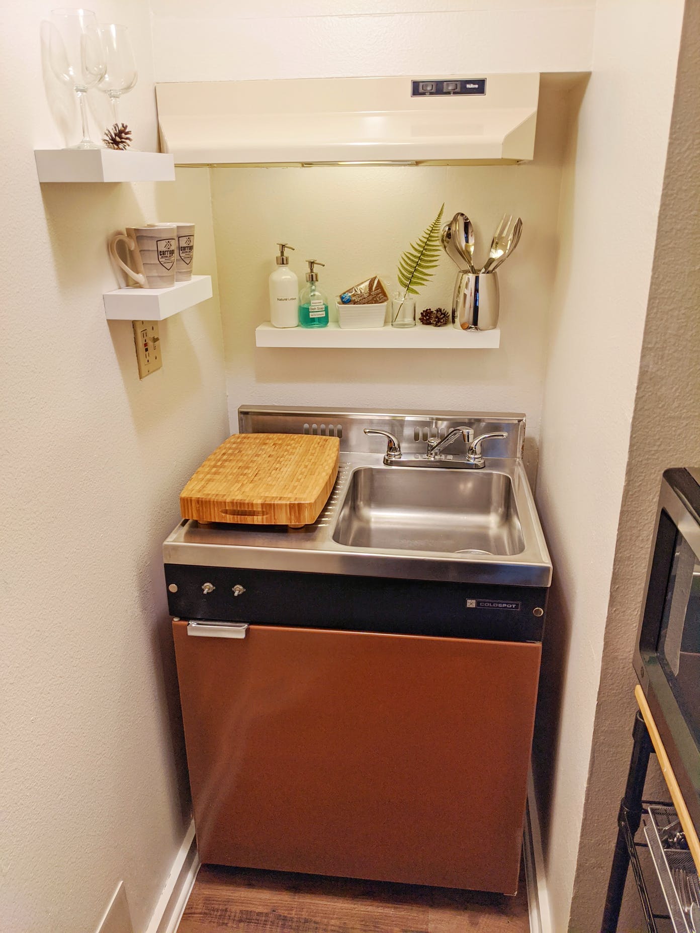 A small kitchen with a sink , dishwasher , and cutting board.