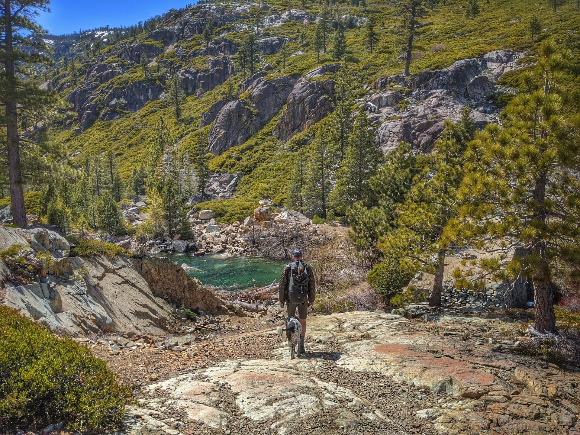 A man is walking on a rocky trail in the mountains near a lake.