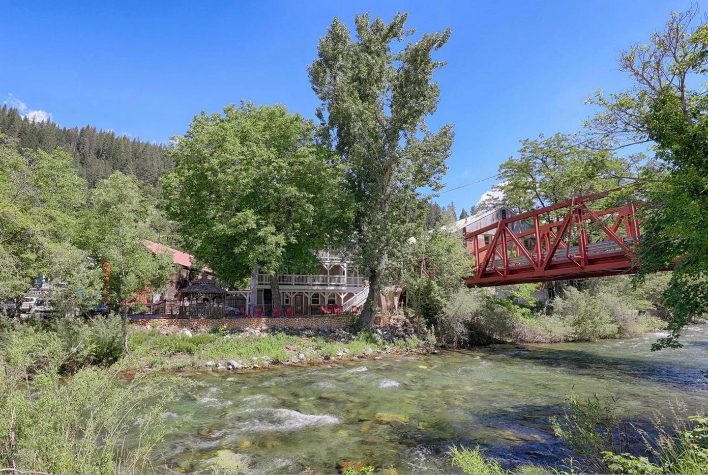 A red bridge over a river with a house in the background.