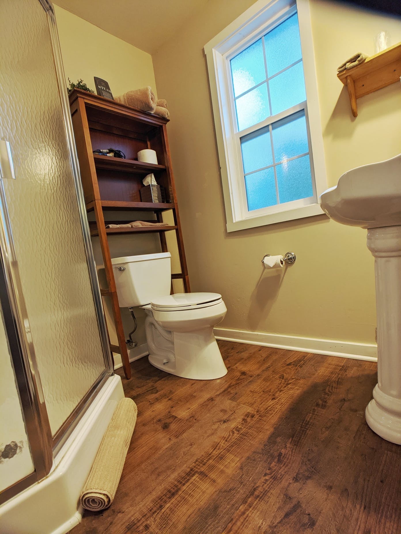 A bathroom with a toilet , sink , shower and window