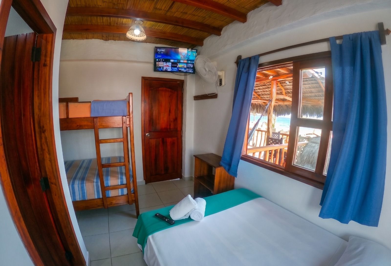 Cozy bedroom with bunk beds, blue curtains, a white bed, TV, and a window overlooking the outdoors