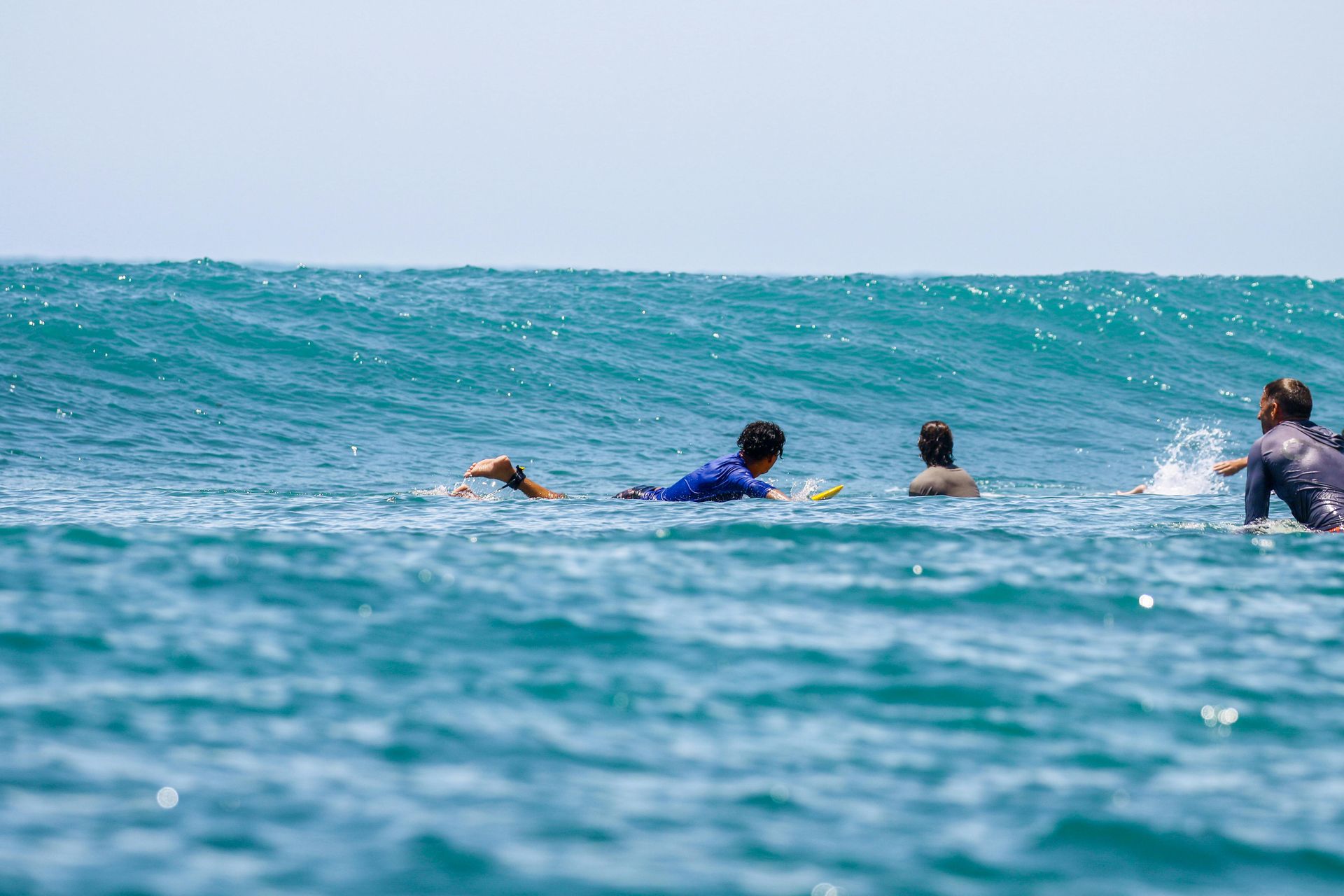 Surfers paddling in blue ocean waves under a clear sky