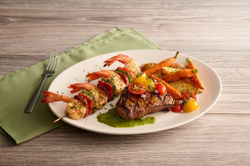 Plated gourmet meal with grilled meat, skewered chicken, and roasted vegetables on a white plate