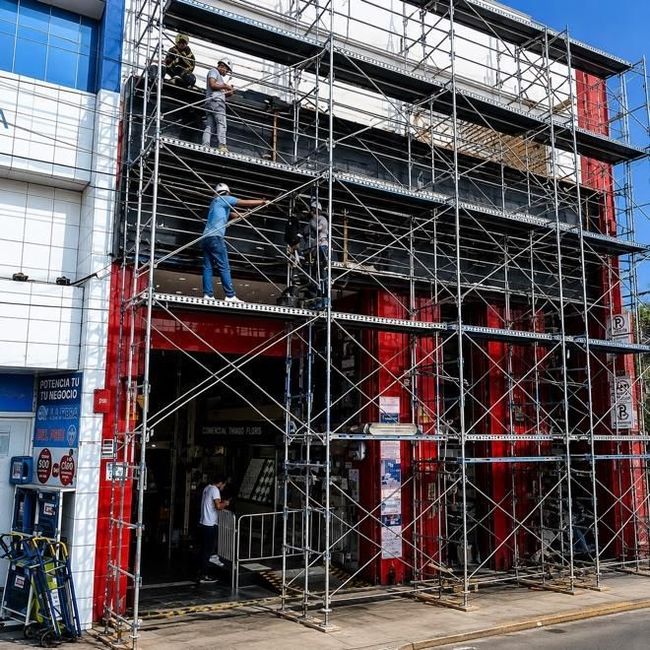 Un andamio cubre la entrada de un edificio rojo y blanco mientras un trabajador permanece de pie sobre la estructura.