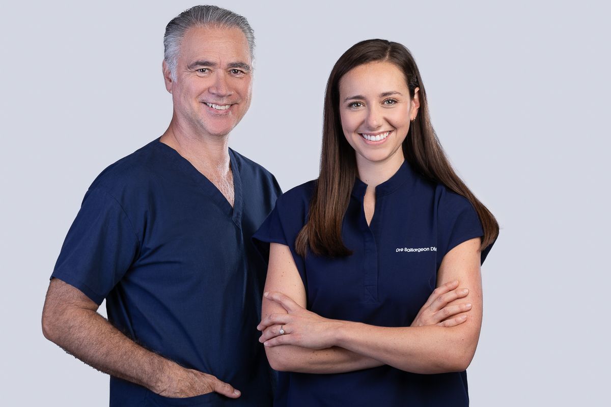 Deux personnes en blouse bleue sourient ; un homme à gauche, une femme à droite, les bras croisés.