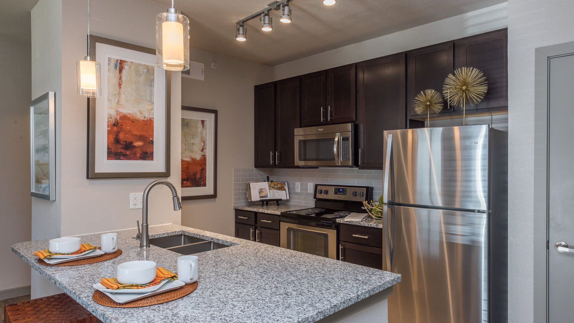 Modern apartment kitchen with granite island, stainless steel fridge, and dark wood cabinets.