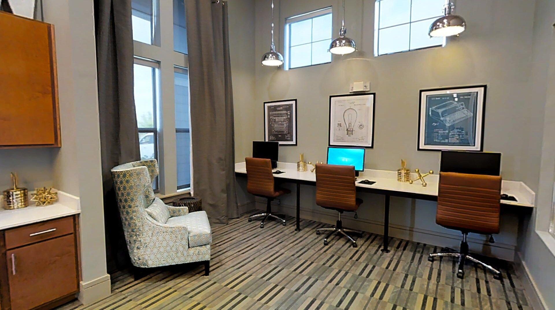 Office-style community workspace with three desks, computers, and framed wall art.