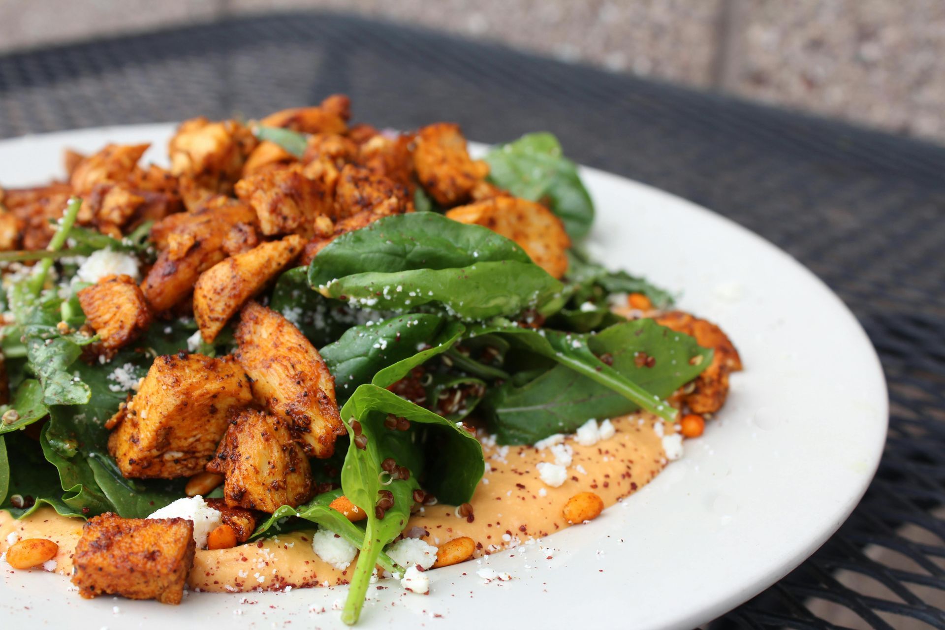A plate of seasoned chicken pieces served over a bed of fresh greens and a creamy orange sauce with sprinkled cheese.