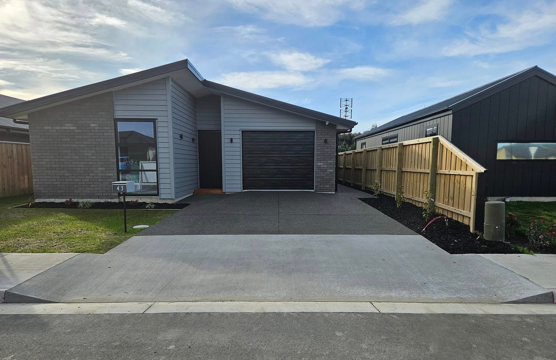 Modern gray house with dark garage door, driveway, and fenced yard; blue sky.