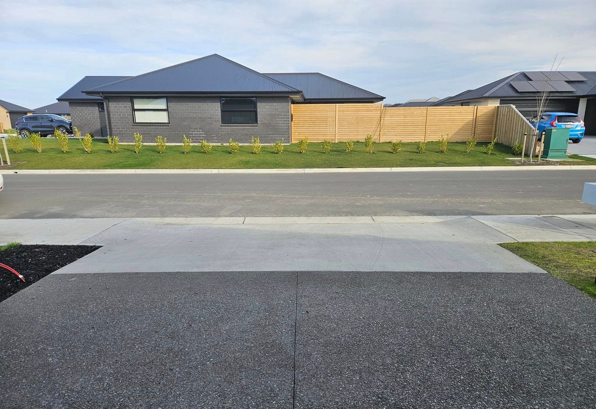 A residential street with a house in the background and a dark paved driveway in the foreground.