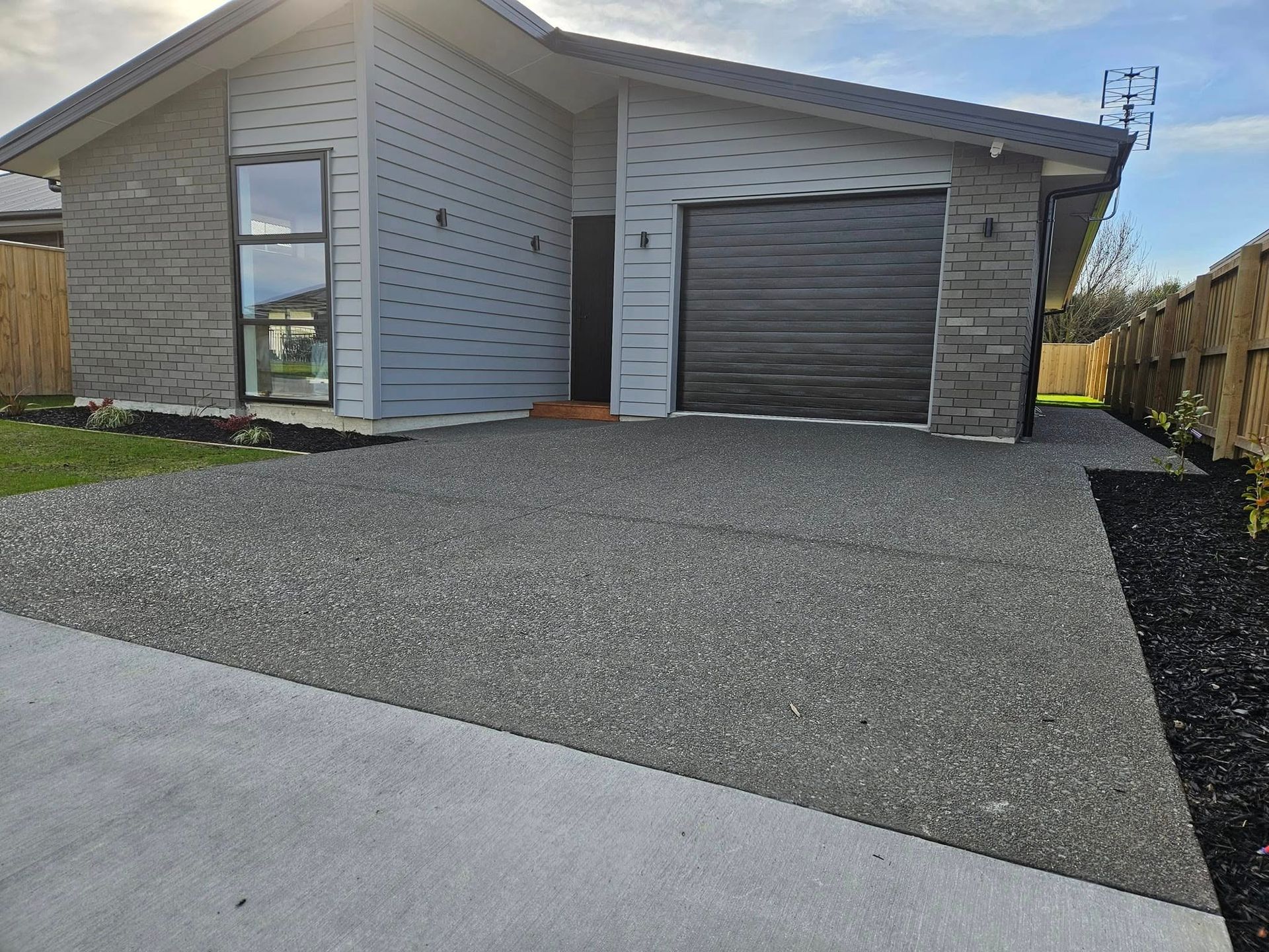 Gray house with dark garage door, stone accents, and dark gravel driveway.