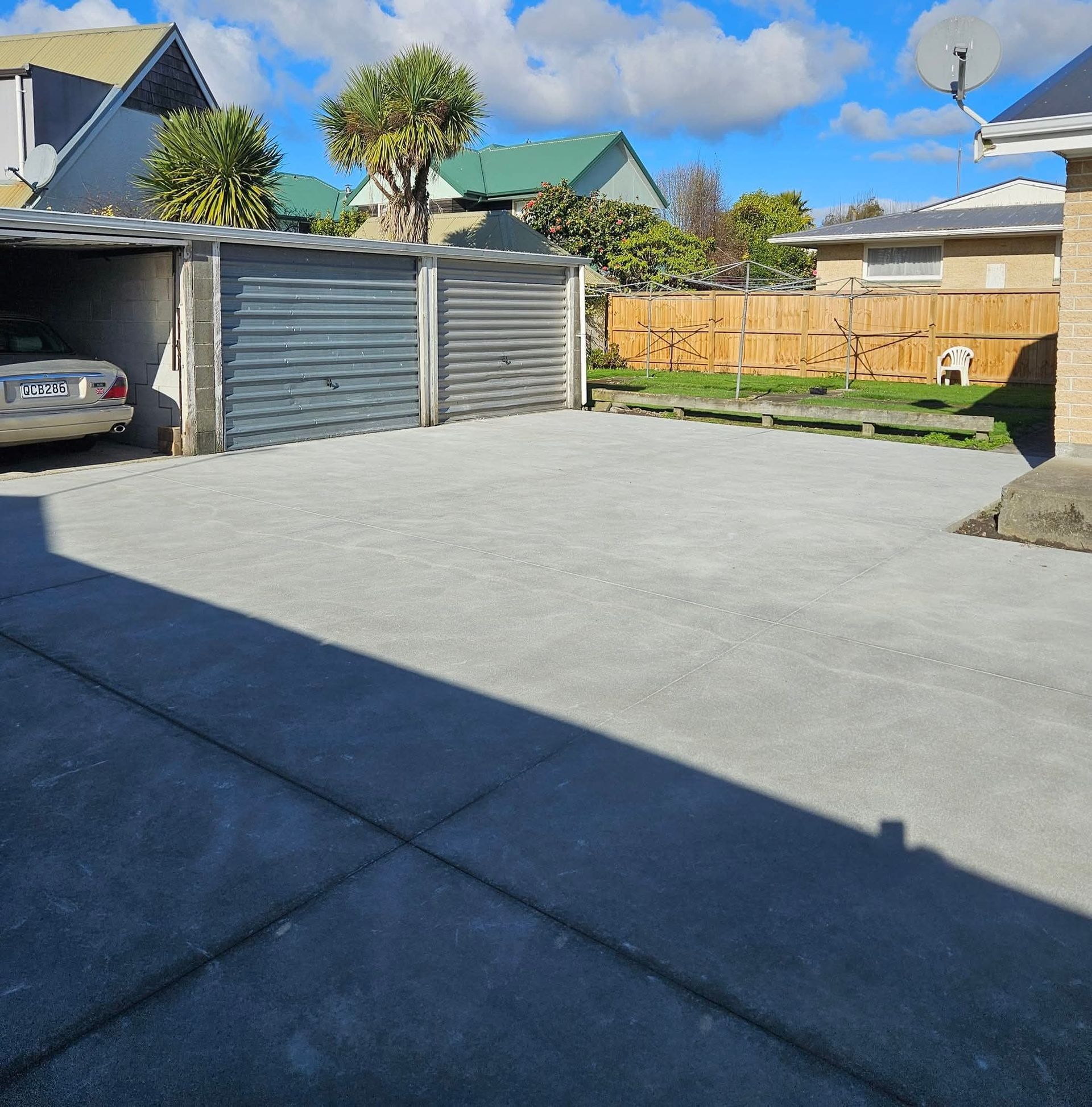 Concrete driveway with two garage doors and a car parked in one, sunny day.