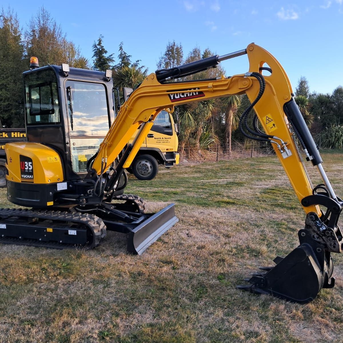 Yellow excavator on grass with black bucket, operating outdoors.