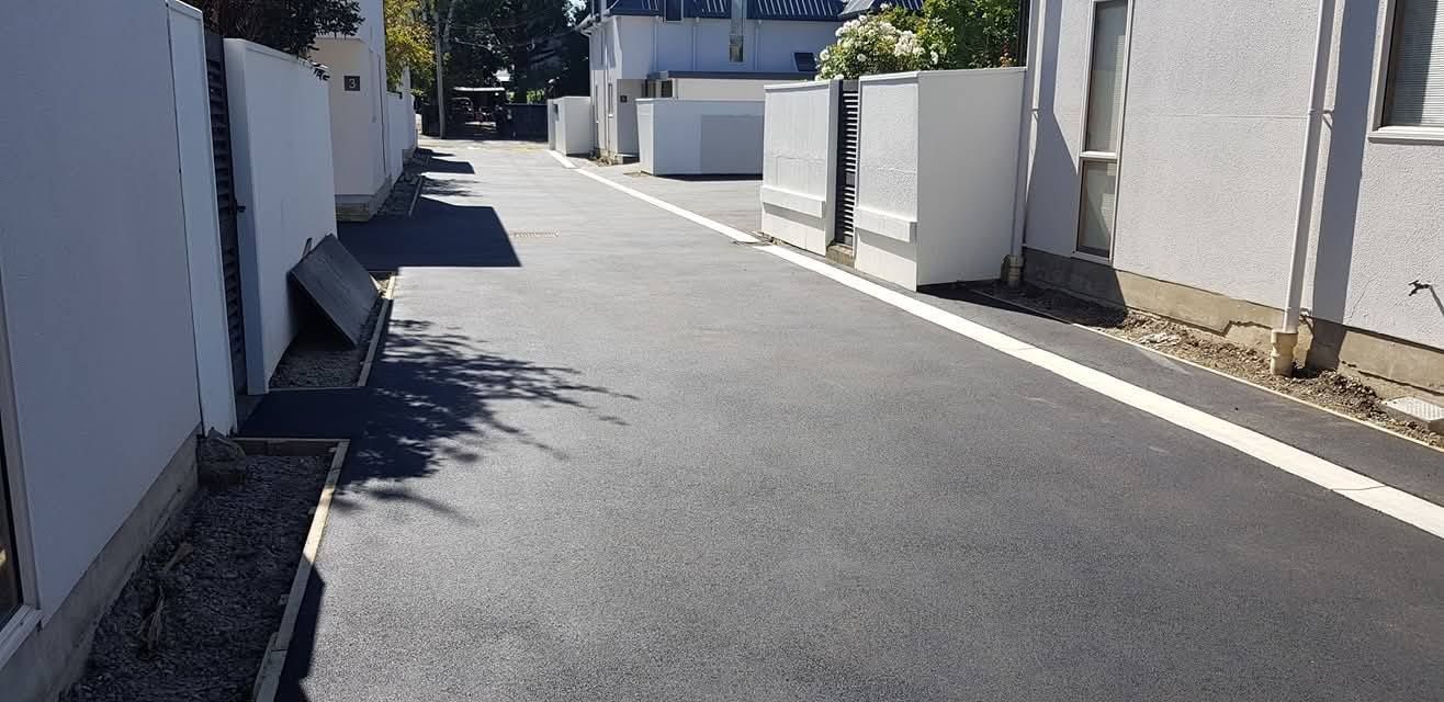An asphalt road lined with white walls and a white stripe. A few white rectangular structures line the road.