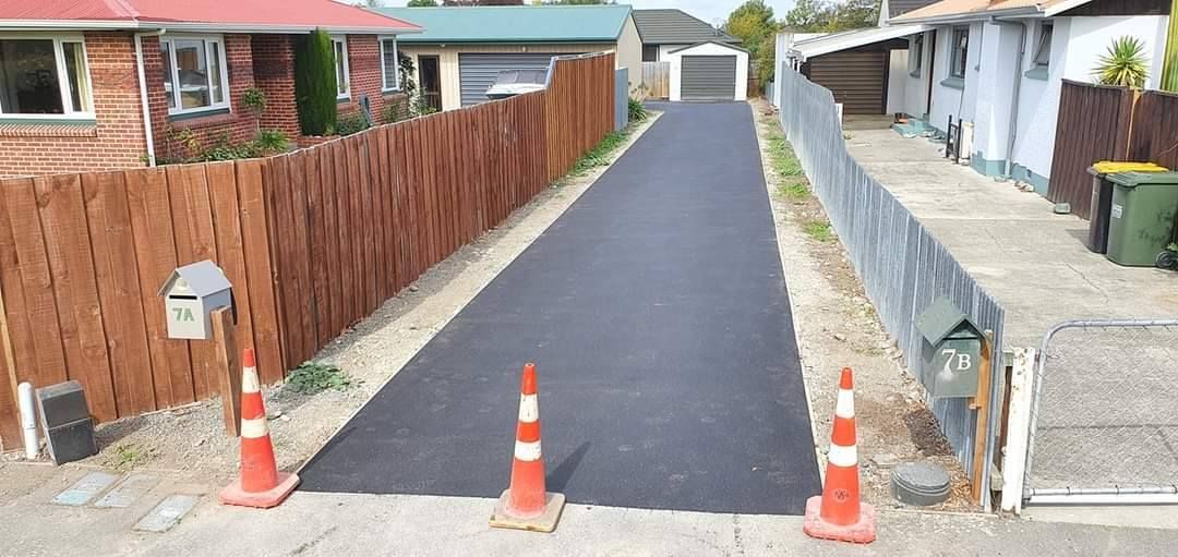 Long paved driveway with orange safety cones; bordered by wooden fence on one side and metal fence on the other.