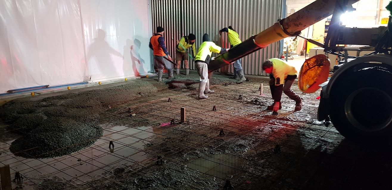 Construction workers pouring concrete on a building site. A truck is dispensing concrete into the work area.