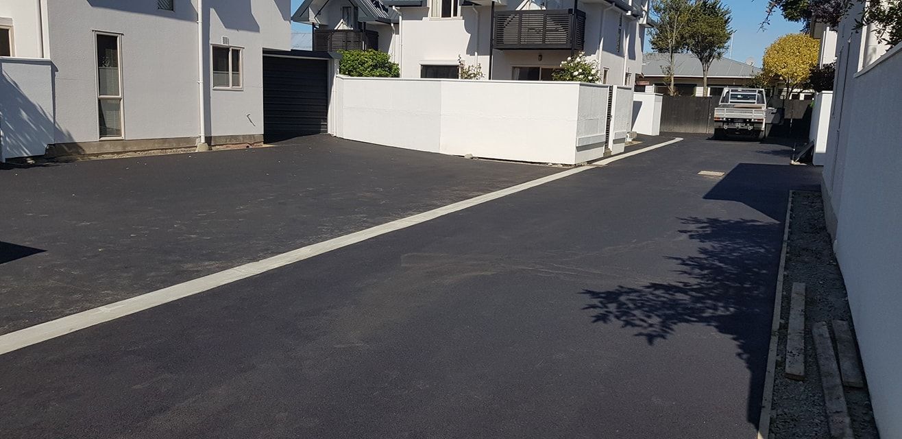 Asphalt road with white line, bordered by white walls and buildings. A truck is parked in the distance.
