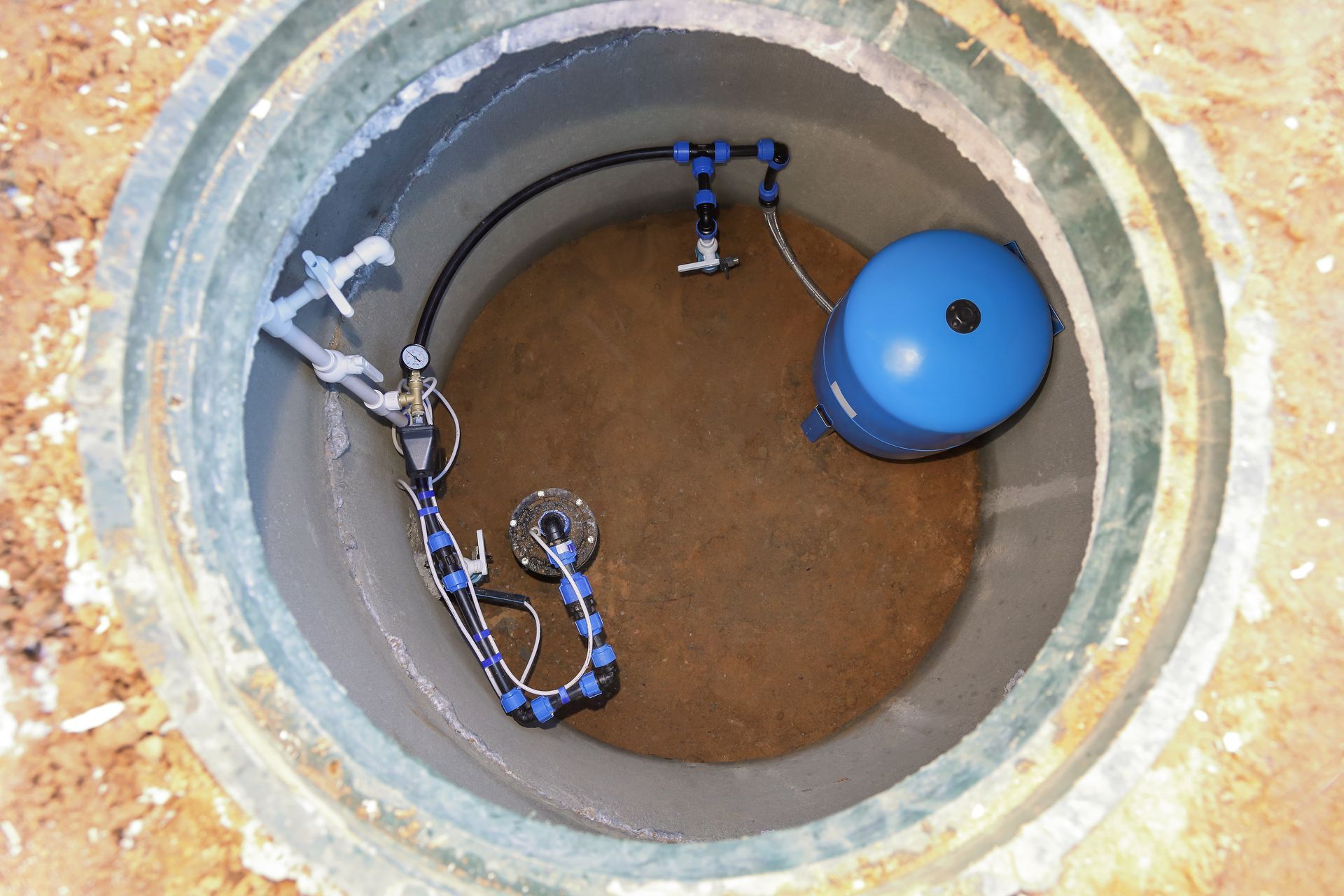 Interior of a well casing with water well pump, pressure tank, and plumbing connections
