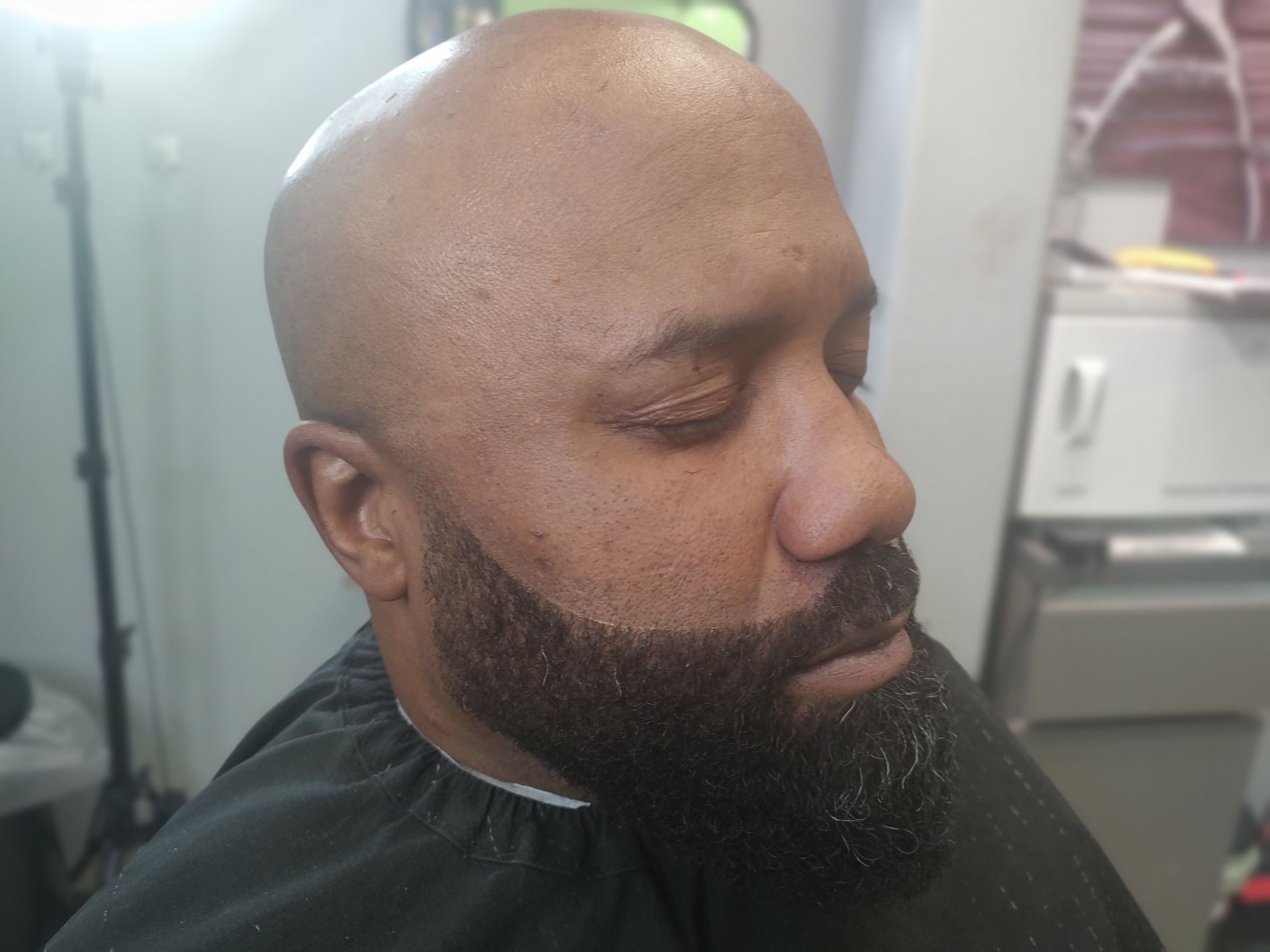 A bald man with a beard is getting his hair cut at a barber shop.