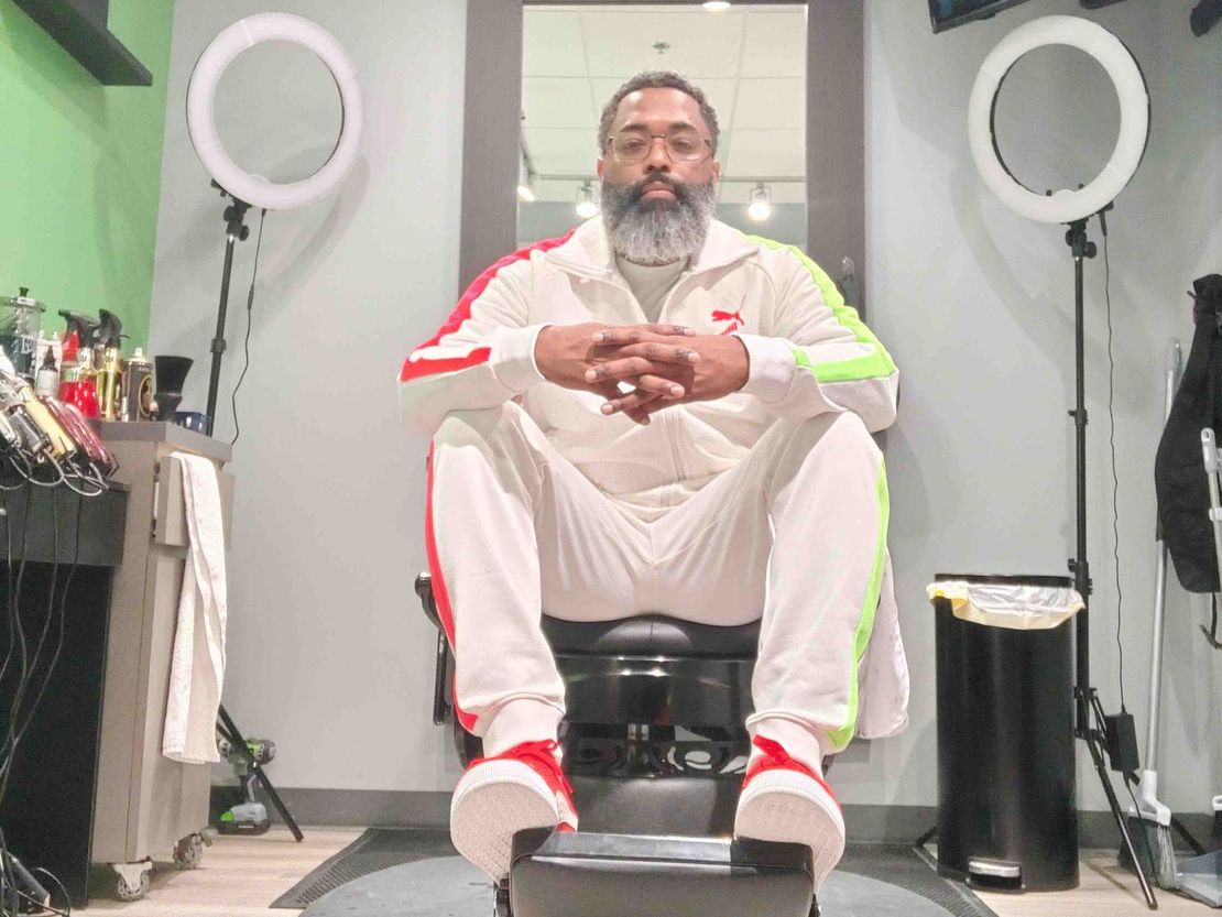 A man is sitting in a barber chair in a barber shop.