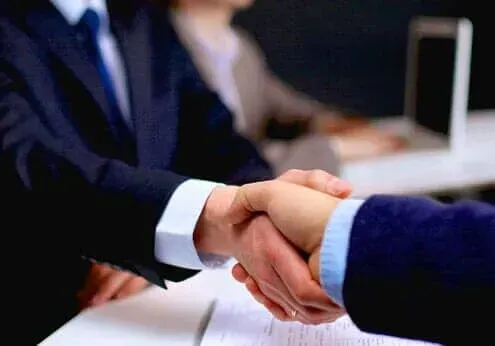 Business handshake between two people in suits at a desk