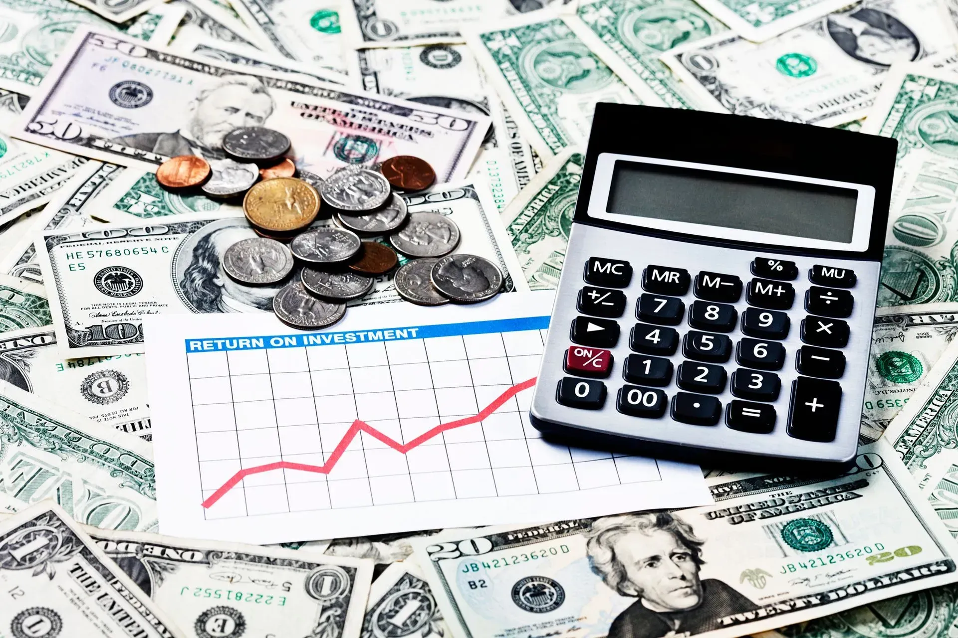 Calculator, coins, and a red line graph on U.S. dollar bills, showing personal finance or budgeting.