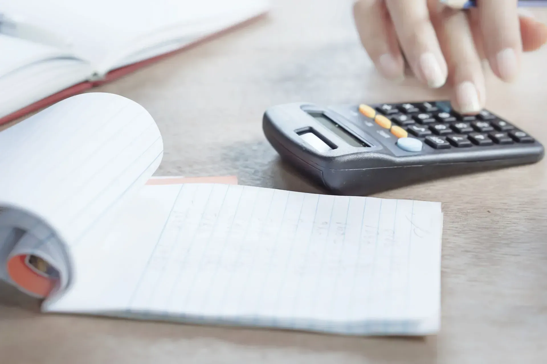 Hand using a calculator beside an open notebook on a desk