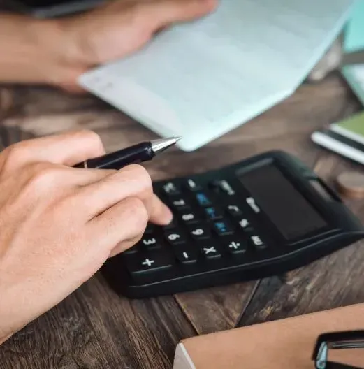 Hand using a calculator and pen over paperwork on a wooden desk