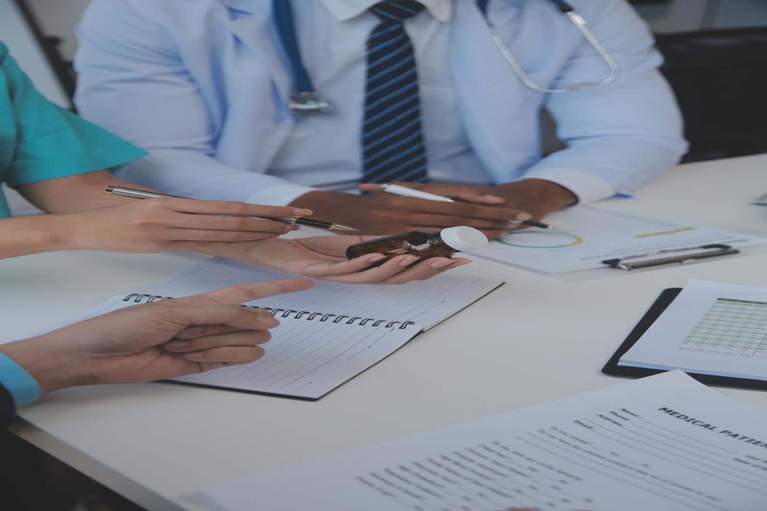 Medical professionals examining medication at a table; medical documents visible.