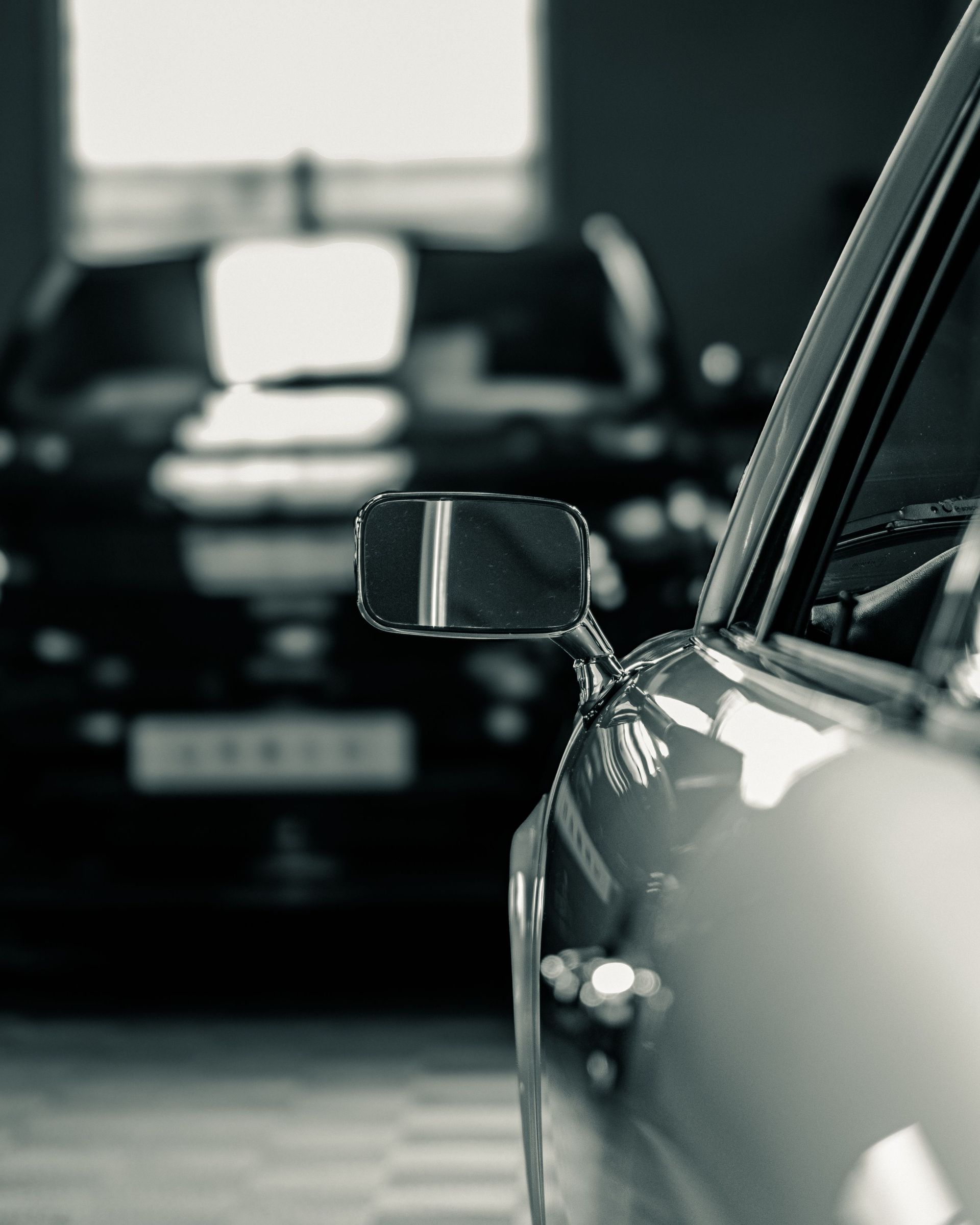 Black and white close-up of a chrome side mirror on a classic sports car