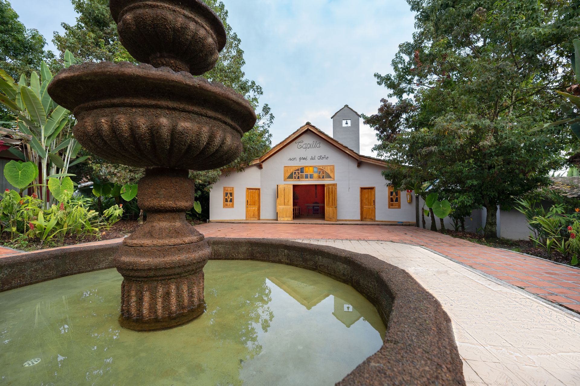 Capilla de Termales El Otoño con fuente en primer plano, fachada blanca y entorno arbolado para ceremonias en Manizales.