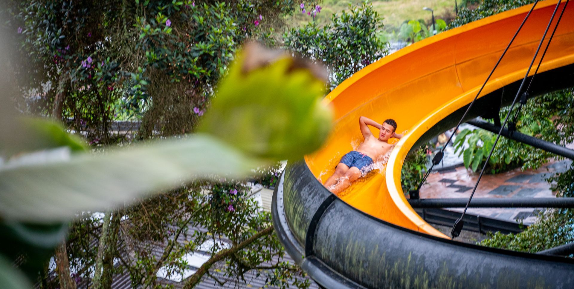 Boy sliding down an orange water slide surrounded by vegetation at a hotel with a water park near Manizales.