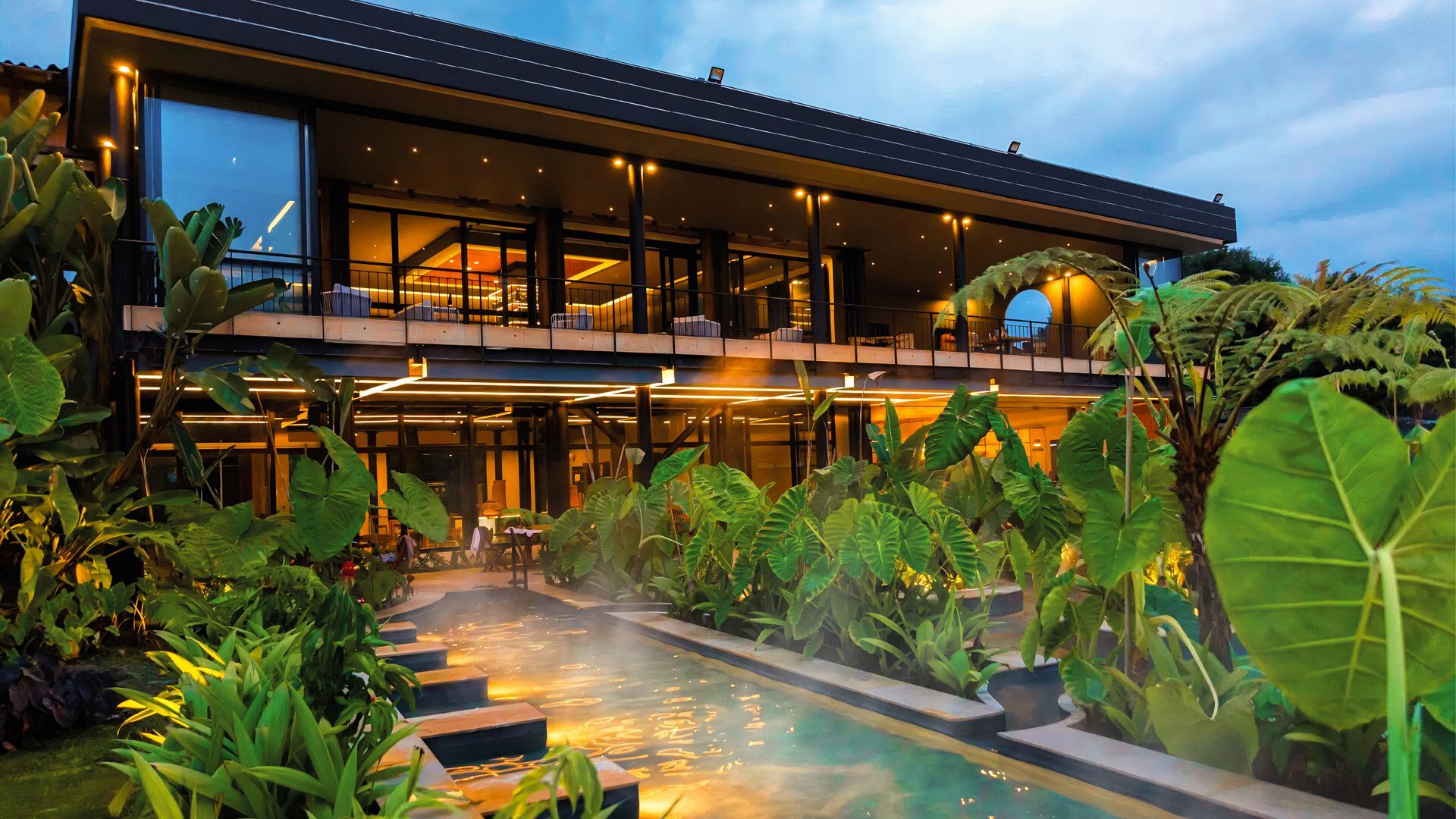 Thermal pool surrounded by vegetation and an illuminated building at Termales El Otoño Manizales.