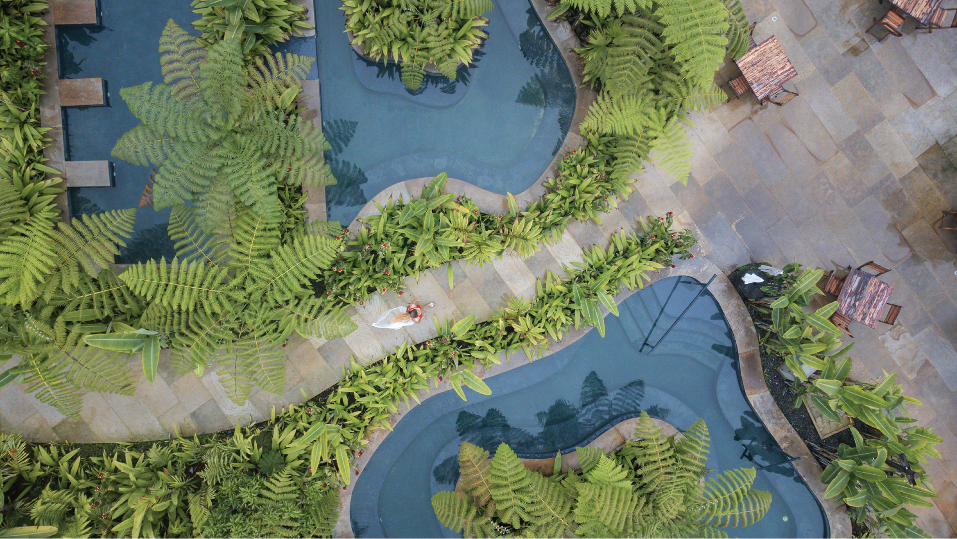 Pools surrounded by vegetation with a woman walking at Termales El Otoño, a hotel with hot springs in Manizales.