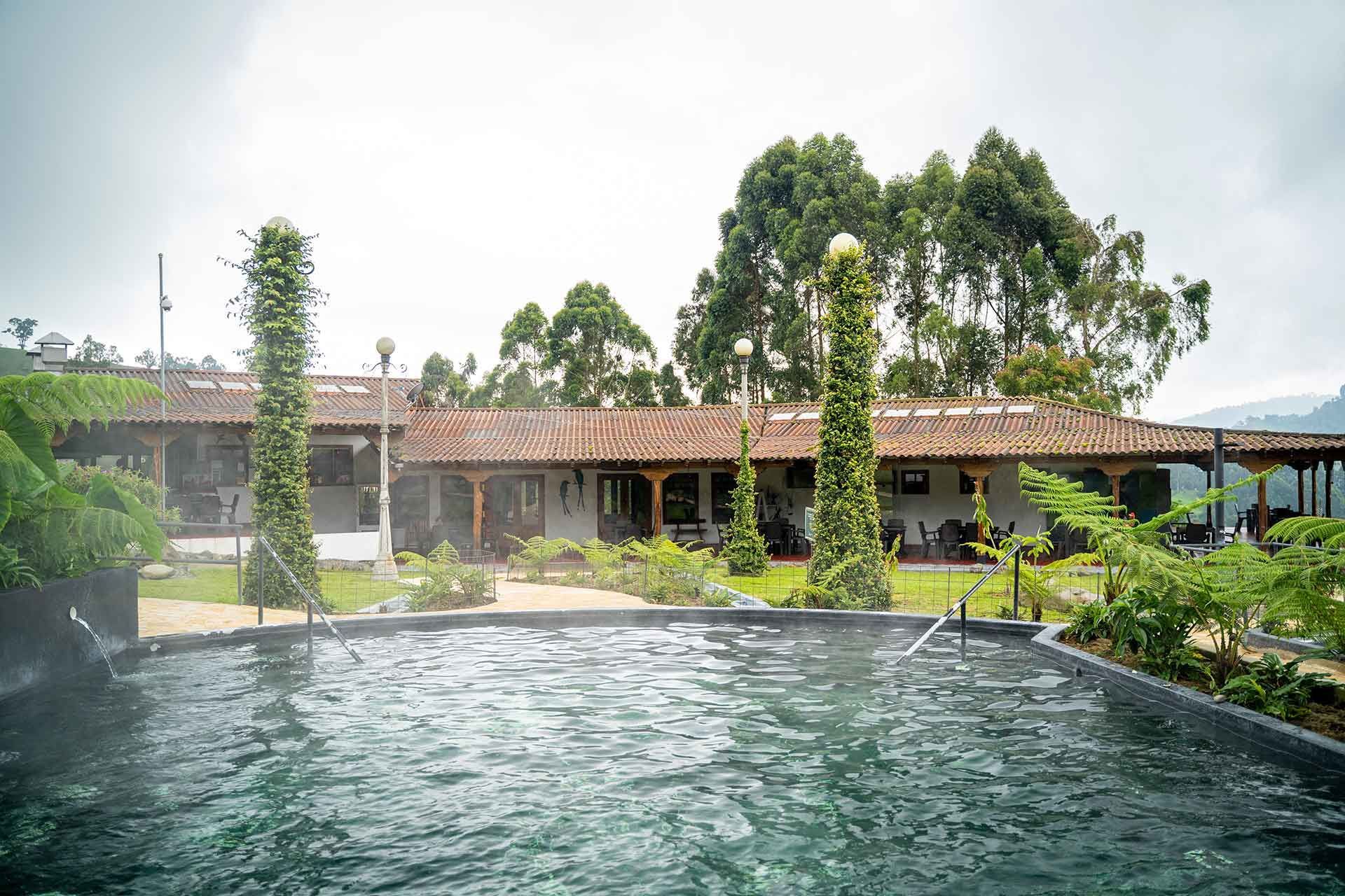 Piscina termal frente a edificio con árboles alrededor en Termales El Otoño, hotel con aguas termales en Manizales.