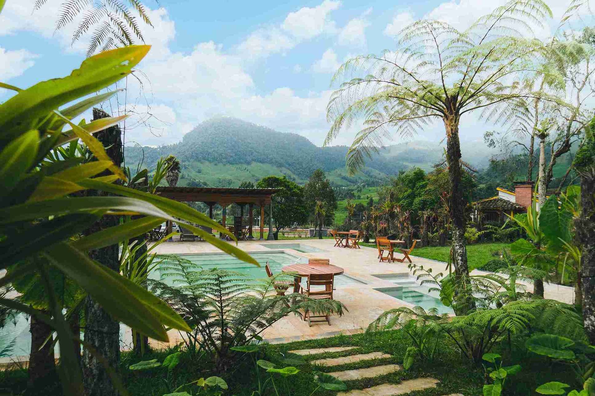 Piscina con mesas, jardines tropicales y vista a la montaña en Termales El Otoño, hotel con aguas termales en Colombia.
