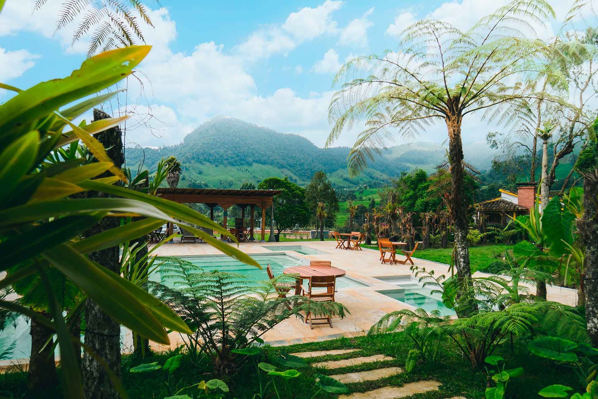 Outdoor pool surrounded by gardens, palm trees, and mountains at Termales El Otoño, a hotel with hot springs in Colombia.